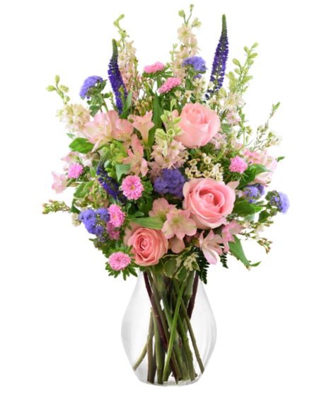 A vibrant floral arrangement featuring pink roses, purple asters, and lush greenery, beautifully displayed in a clear glass vase.